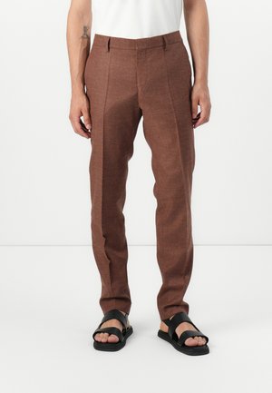 Brown tailored pants with a textured fabric, featuring a slim fit, creases, and a flat waistband. Paired with black flat sandals.
