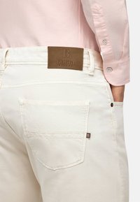 Bele jeans iz bombažem z usnjeno oznako BOGGI Milano na hrbtu. Imajo žep na zaklopu in subtilne šive.
