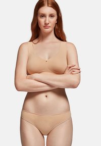 Sostén nude con tirantes anchos y una textura suave, combinado con braguitas de corte bajo a juego. Diseño sencillo con un pequeño acento decorativo en el centro.