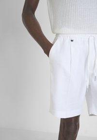 Shorts en lin blanc avec une coupe décontractée, dotés d'une taille élastique, d'un cordon de serrage, de poches latérales et de plis subtils à l'avant.