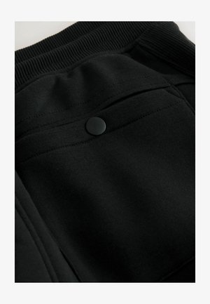 Sorte sweatpants med et ribbet taljebånd, knaplukning og en pyntelomme bagpå, lavet i et glat stof.