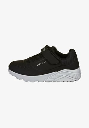 Scarpe sportive nere con superiore in materiale sintetico liscio, chiusura con lacci e strap in velcro, e suola in gomma bianca con scanalature testurizzate.
