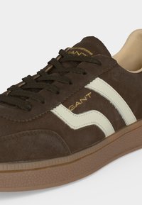Baskets en daim marron avec bande latérale blanche, lacets noirs, marquage "GANT" et semelle en caoutchouc marron texturée.