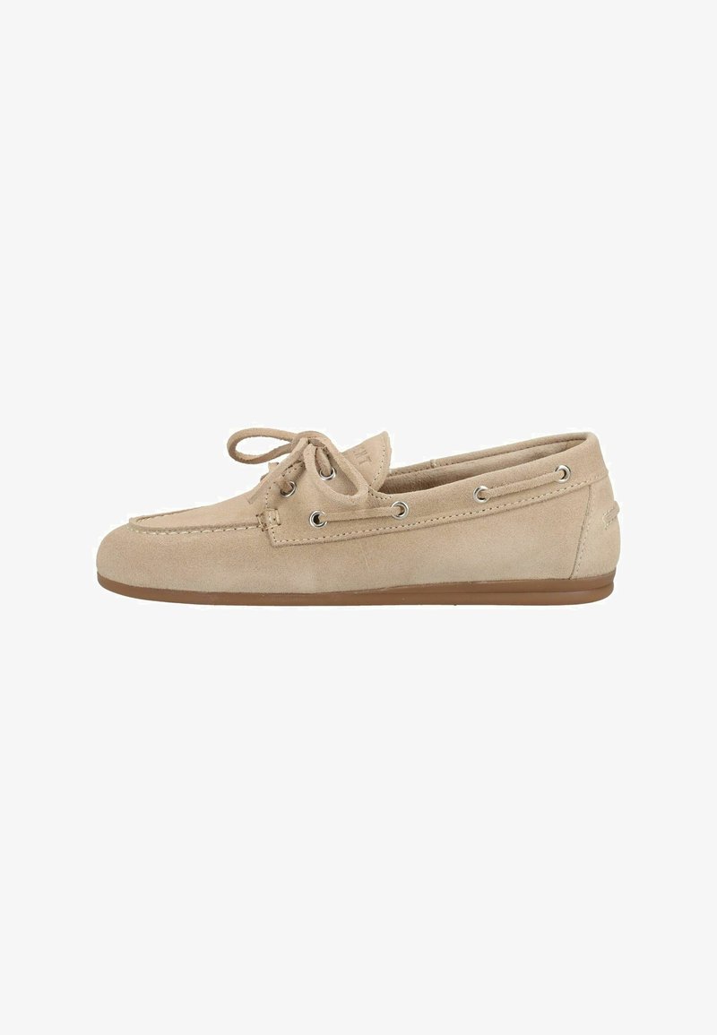 Beige mokkasino-loafer i ruskind med snørebånds sløjfe, metaløjer og lav brun flad sål, set fra siden.