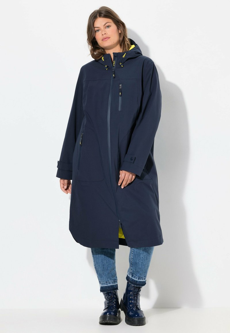 Manteau imperméable bleu marine avec fermeture éclair à l'avant, grande capuche, cordons de serrage ajustables et poches latérales ; doublé à l'intérieur d'un jaune vif.