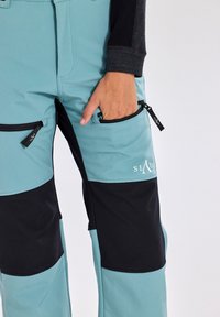 Sporty pants in teal and black, featuring a zipper pocket, made of durable material with a smooth texture, designed for outdoor activities.
