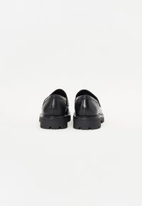 Mocasines de cuero negro con punta redonda y suela de goma gruesa. Textura suave con sutiles detalles de costura en el empeine.