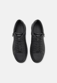 Musthave must be syntetiilisest nahast tennised, millel on sile viimistlus, lace-up disain, külgmine tõmblukk ja tekstuurilised aktsendid väliskülgedel.