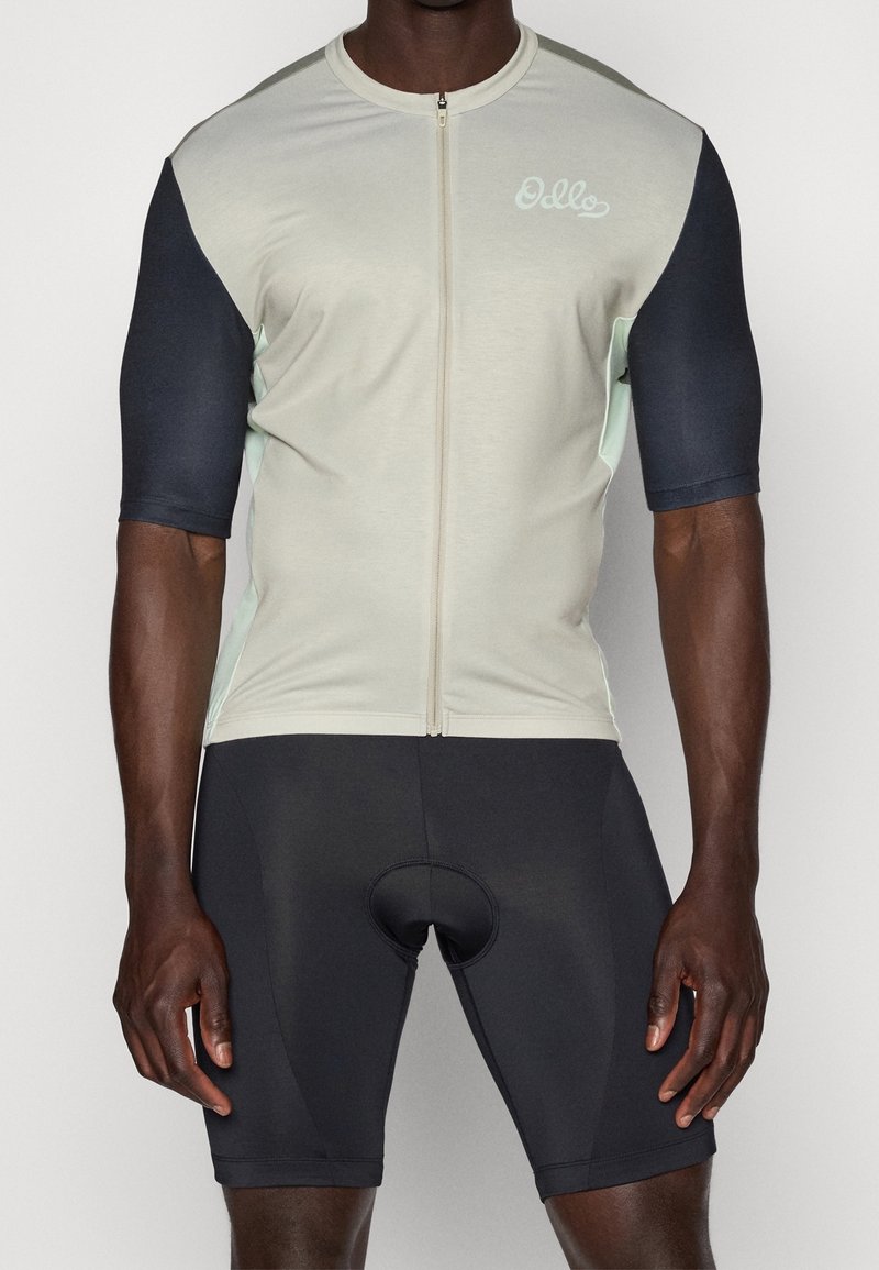 Camisa de ciclismo gris claro con mangas cortas en marino y cremallera, combinada con pantalones cortos negros que tienen una zona acolchada. Tela lisa y elástica.