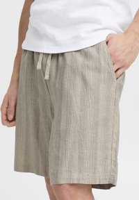 Lightweight, striped shorts in beige and gray fabric, featuring a drawstring waist and side pockets. Casual and breathable design.