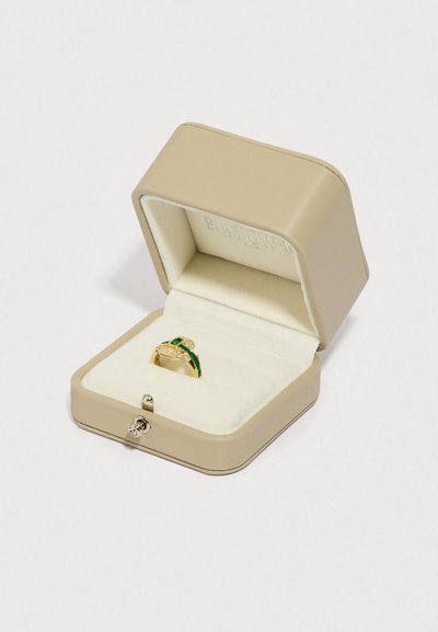Χρυσό δαχτυλίδι με πράσινες λεπτομέρειες και διαυγή πετράδια σε μπεζ κουτί κοσμημάτων επενδεδυμένο με βελούδο. Το κουτί διαθέτει λεία υφή και διακοσμητικό κούμπωμα.