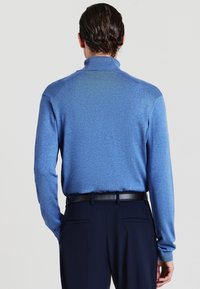Blauer Strickpullover mit einem gerippten Kragen, geraden Ärmeln und einer glatten Textur. Kombiniert mit dunklen Hosen mit einem Gürtel.