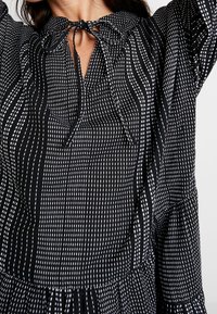 Blusa a rayas en blanco y negro con un nudo en el cuello, que presenta un corte holgado, mangas largas y un dobladillo con volantes.