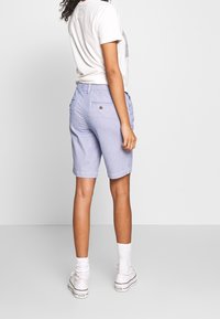 Pantalones cortos a rayas de color azul claro con un corte ajustado, bolsillos delanteros y traseros, y un detalle de botón en el bolsillo trasero. Combinados con zapatillas blancas.
