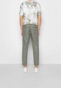 Šedé tričko Reebok s motivem palmy na zadní straně, spárované se světle zelenými kalhotami a bílými botami. Volný střih a lehký materiál.