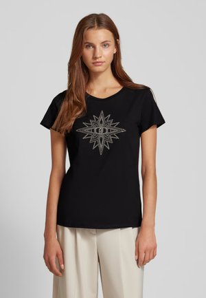 Maglietta nera con un design a raggi di sole argentati sul davanti, maniche corte, scollatura rotonda, realizzata in un tessuto morbido. Pantaloni di colore crema.