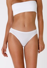 Slip bikini bianchi in cotone con una texture liscia, taglio basso e cintura elastica, caratterizzati da linee semplici e pulite senza decorazioni.