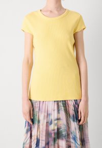 Žluté žebrované tričko s krátkými rukávy a kulatým výstřihem. Měkká textura s přiléhavým střihem, spárované s barevnou plisovanou sukní.
