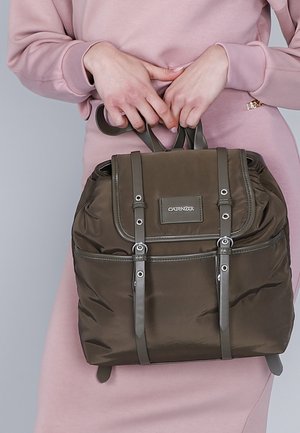 Zaino in nylon marrone con forma strutturata, spallacci regolabili, dettagli argentati e un pattina frontale con logo. Texture liscia.