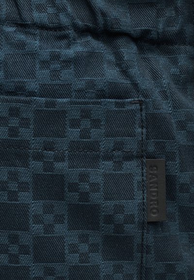 Σκούρο μπλε ύφασμα με υφασμένη γεωμετρική καρό υφή και ραμμένη μαύρη ετικέτα με την επιγραφή "SANDRO".