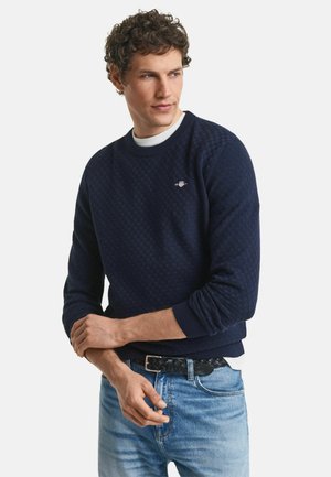 Sudadera de punto azul marino con un patrón de cuadros texturizado, puños acanalados y cuello redondo, que presenta un pequeño logo en el lado izquierdo del pecho.