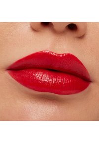 Bright red lipstick applied to well-defined lips; glossy finish with smooth texture and subtle lines visible on the surface.