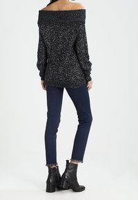 Suéter negro de punto con hombros al descubierto y tela texturizada, combinado con jeans de un azul oscuro y botas negras por encima del tobillo, con un tacón grueso.