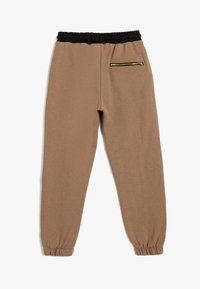 Brune svedpants med en sort elastisk talje, tapered ben og en guld lynlåslomme på ryggen. Blødt stof med en glat tekstur.