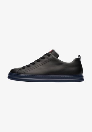 Sort lædersneaker med rund tå, flad snøring og en tykkere navy gummisål. Har diskrete perforeringer og en hælflap.
