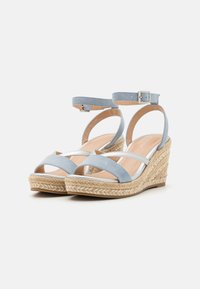Les sandales à talons compensés présentent un dessus en suédine bleue avec des accents blancs, une bride au niveau de la cheville et une plate-forme en jute tressé. Design ouvert à l'avant arrondi.