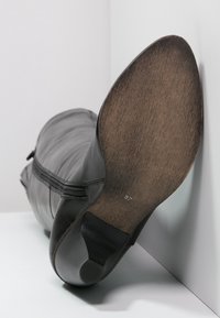 Botte en cuir noir avec fermeture éclair sur le côté, bout effilé et semelle texturée imitant le bois. Taille 37 visible sur la semelle intérieure.