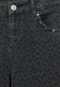 Gros plan sur un pantalon en denim noir avec un imprimé léopard sombre subtil, bouton argenté, rivets et détails de poche avant.