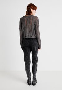 Grijze cropped trui met een textuur gebreide stof en versleten details, gecombineerd met hooglopende zwarte jeans en enkellaarsjes.