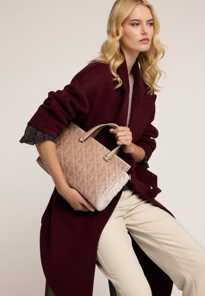 Borsa rosa chiaro testurizzata con motivo floreale trapuntato, doppi manici e chiusura con zip, tenuta contro un cappotto bordeaux scuro.