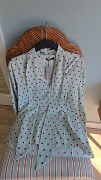 Jasnoniebieska bluzka w czerwone kropki, z dekoltem w kształcie litery V i zapinana na guziki z przodu. Miękka tkanina luźno opada, z rozkloszowanym dołem.