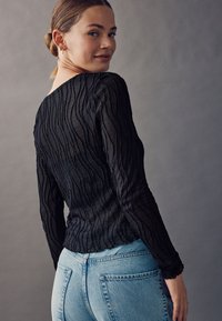 Schwarzes, strukturiertes Langarmoberteil mit wellenförmigen Streifen, kombiniert mit hellblauen, hoch taillierten Jeans. Glatter Stoff, figurbetontes Design, dezente Akzente.