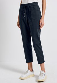 Pantalones cropped azul marino hechos de una tela suave y transpirable; cuentan con una cintura elástica con cordón y bolsillos frontales. Se llevan con zapatillas blancas.