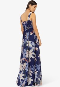 Abito lungo floreale blu navy con bodice arricciato, spalline larghe e gonna fluttuante decorata con grandi motivi di fiori bianchi e rosa.