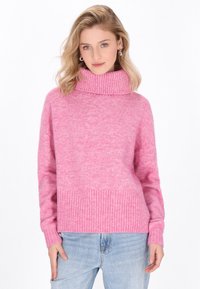 Rosa Rollkragenpullover mit geripptem Saum und Bündchen, aus weichem Stoff gefertigt, mit einem lockeren Schnitt und strukturiertem Finish. Kombiniert mit hellblauen Jeans.