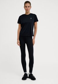 Sort atletisk t-shirt med korte ærmer og rund halsudskæring, kombineret med sorte leggings og sorte sneakers. Minimalistisk design og strækbart materiale.