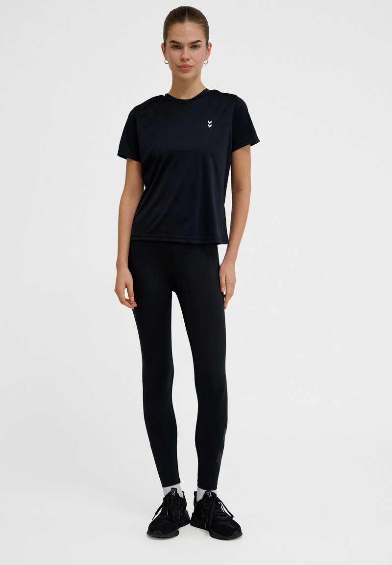 Sort atletisk t-shirt med korte ærmer og rund halsudskæring, kombineret med sorte leggings og sorte sneakers. Minimalistisk design og strækbart materiale.