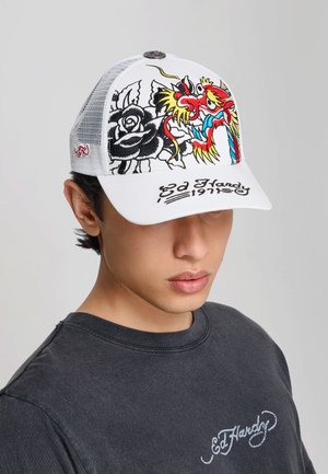 Ung mand iført en hvid netkasket med broderet drage, sort rose og teksten "Ed Hardy 1971", kombineret med en sort Ed Hardy t-shirt.