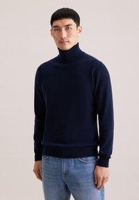 Pull à col roulé marine fabriqué en tissu doux, avec un design ajusté, un col et des poignets côtelés, une texture lisse et peu de détails.