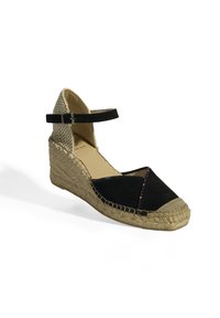 Espadrille compensée en suède noir avec une semelle en jute tissée, dotée d'une sangle de cheville réglable et d'un design croisé accentué par un détail brillant.
