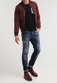 Bordeaux bomberjakke over en sort t-shirt, parret med slidte blå jeans og bordeaux ankel støvler.