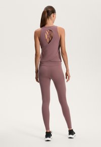 Athletic dual-tone tank top and leggings in mauve, featuring a layered design with a detailed open back. Black athletic shoes complete the look.