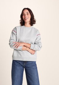 Gray sweatshirt with round neckline and red stitching accents on sleeves. Pair of blue wide-leg jeans completes the outfit. Smooth texture.