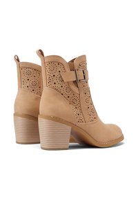 Stivaletti alla caviglia color tan con design perforato, tacco piatto e accento di fibbia visibile. Texture in morbido camoscio e forma della punta arrotondata.
