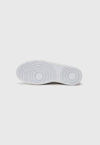 Sola de ténis branca com padrões de pega circulares e pequenos logos. Textura lisa, feita de um material de borracha flexível e durável.