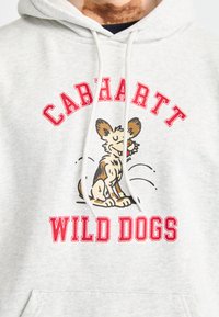 Sudadera gris con un gráfico de perro de dibujos animados, texto rojo que dice "CARHARTT" y "WILD DOGS", con un bolsillo frontal y capucha con cordón.